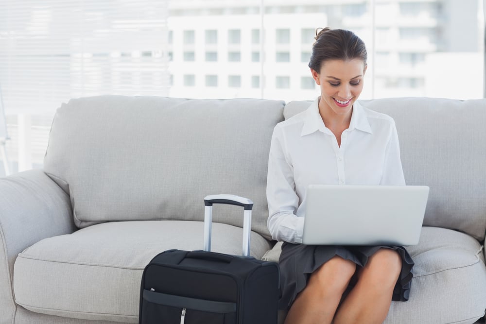 Businesswoman sitting on the couch using laptop beside her suitcase