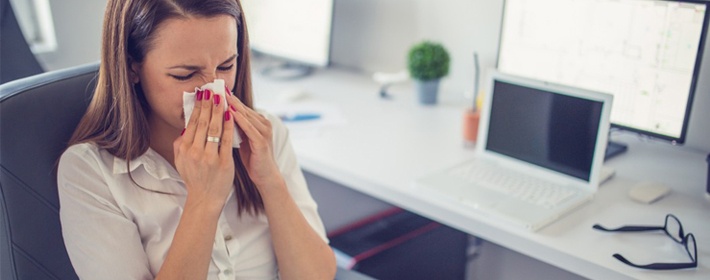 Woman blowing nose indoors at desk
